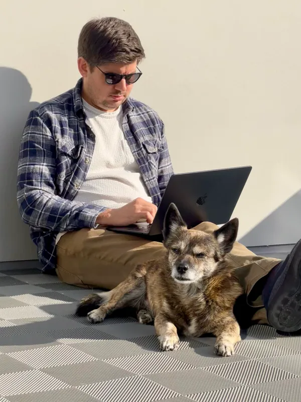 Kyle Evans working on a laptop in the sunshine with a dog at his feet.